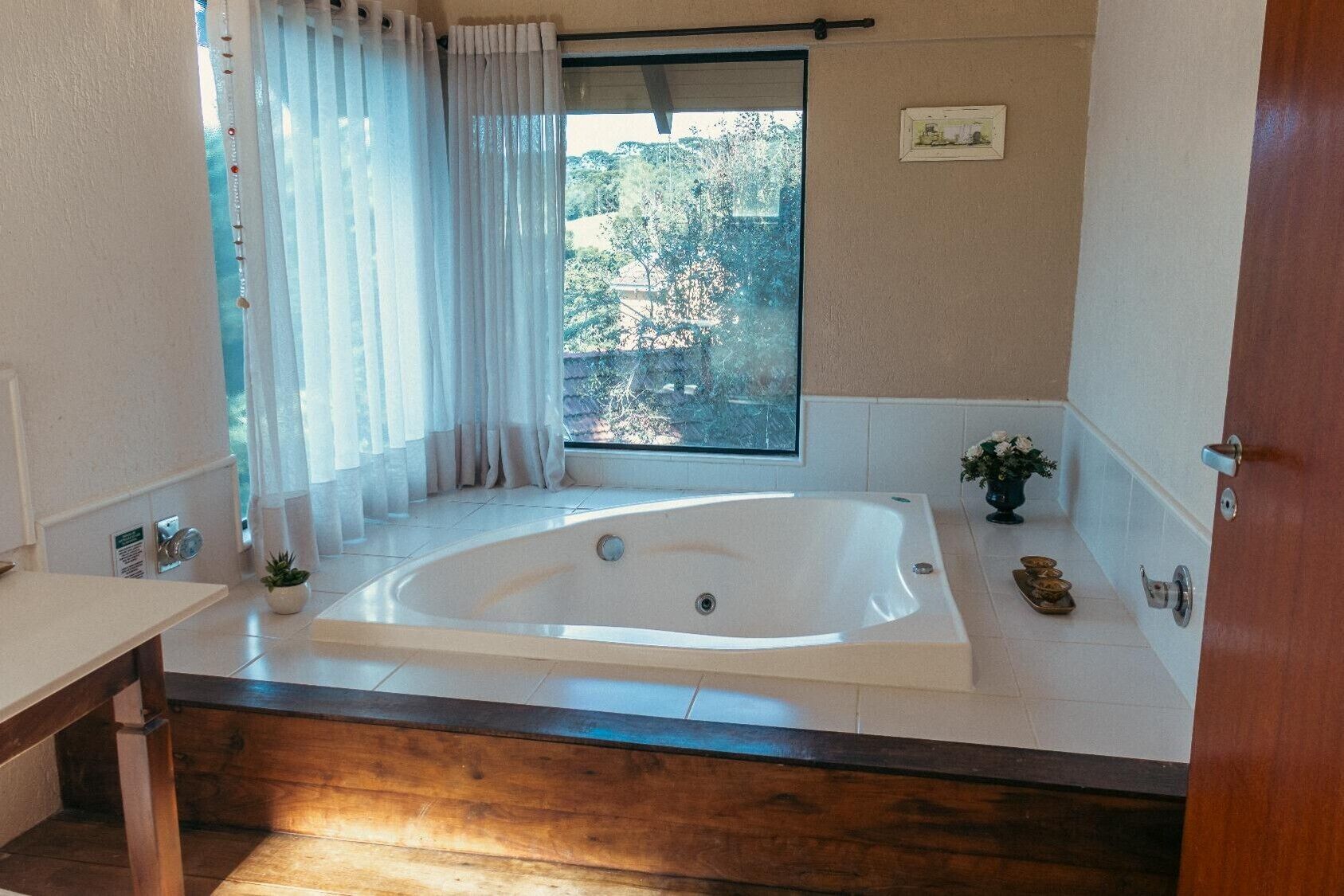 Un baño moderno con una bañera grande, una ventana que da a árboles y una planta pequeña en el mostrador.