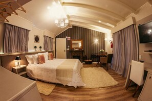 A hotel room with a large bed, a TV, a fireplace, and a dining area. - Serra Bela Eco Pousada (Urubici)