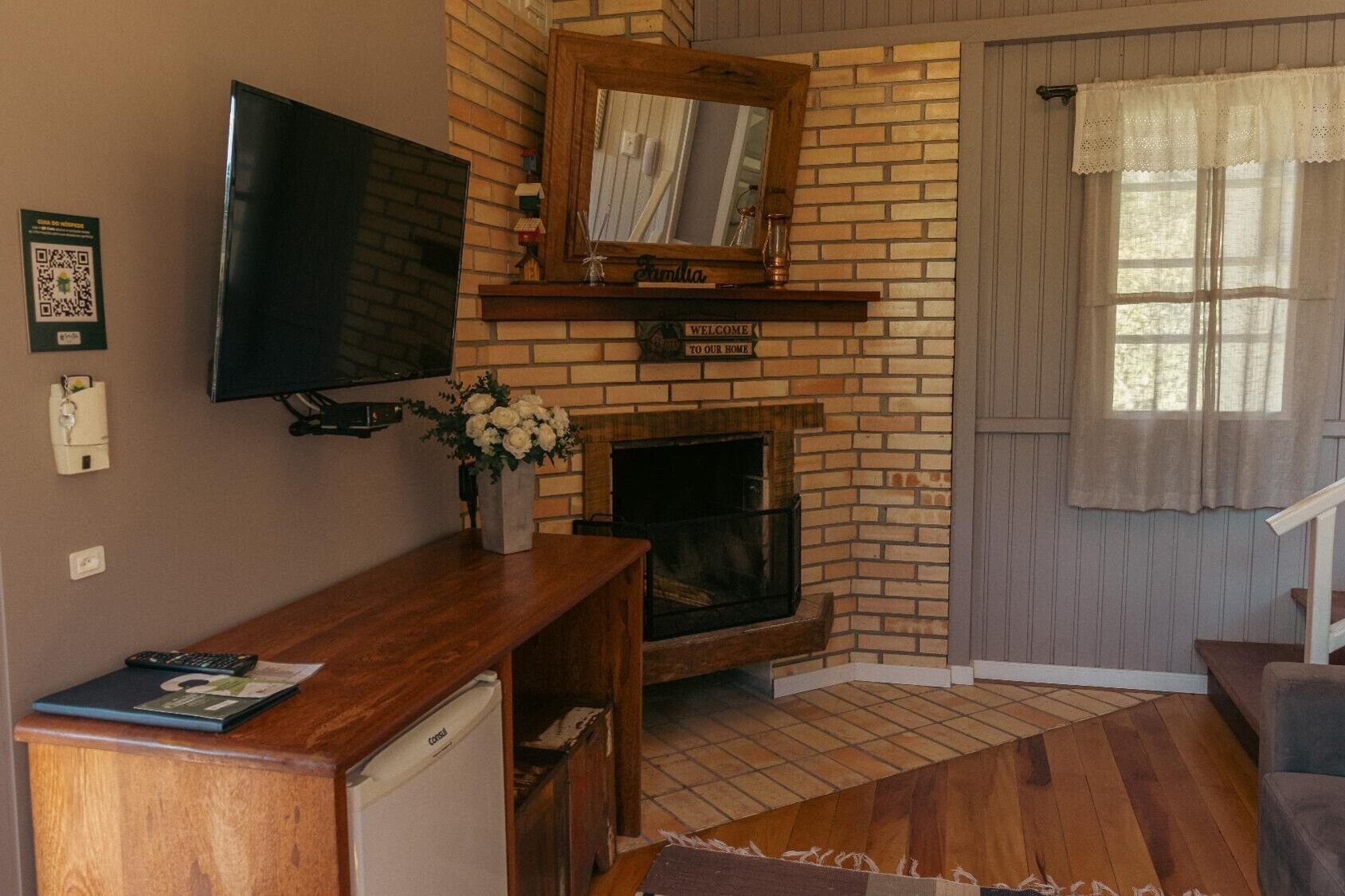 A cozy living room with a brick fireplace, a flat-screen TV mounted on the wall, a wooden coffee table, and a comfortable chair.