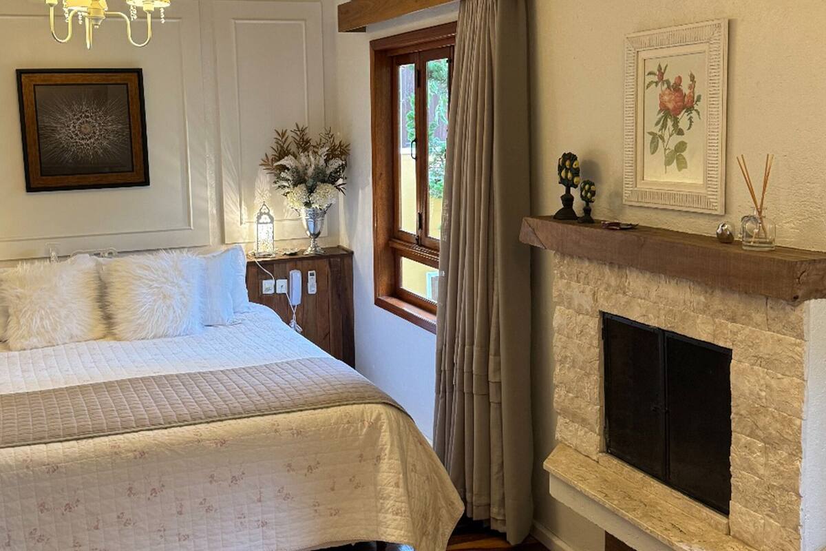 A bedroom with a bed, a chandelier, a fireplace, and a window with curtains.