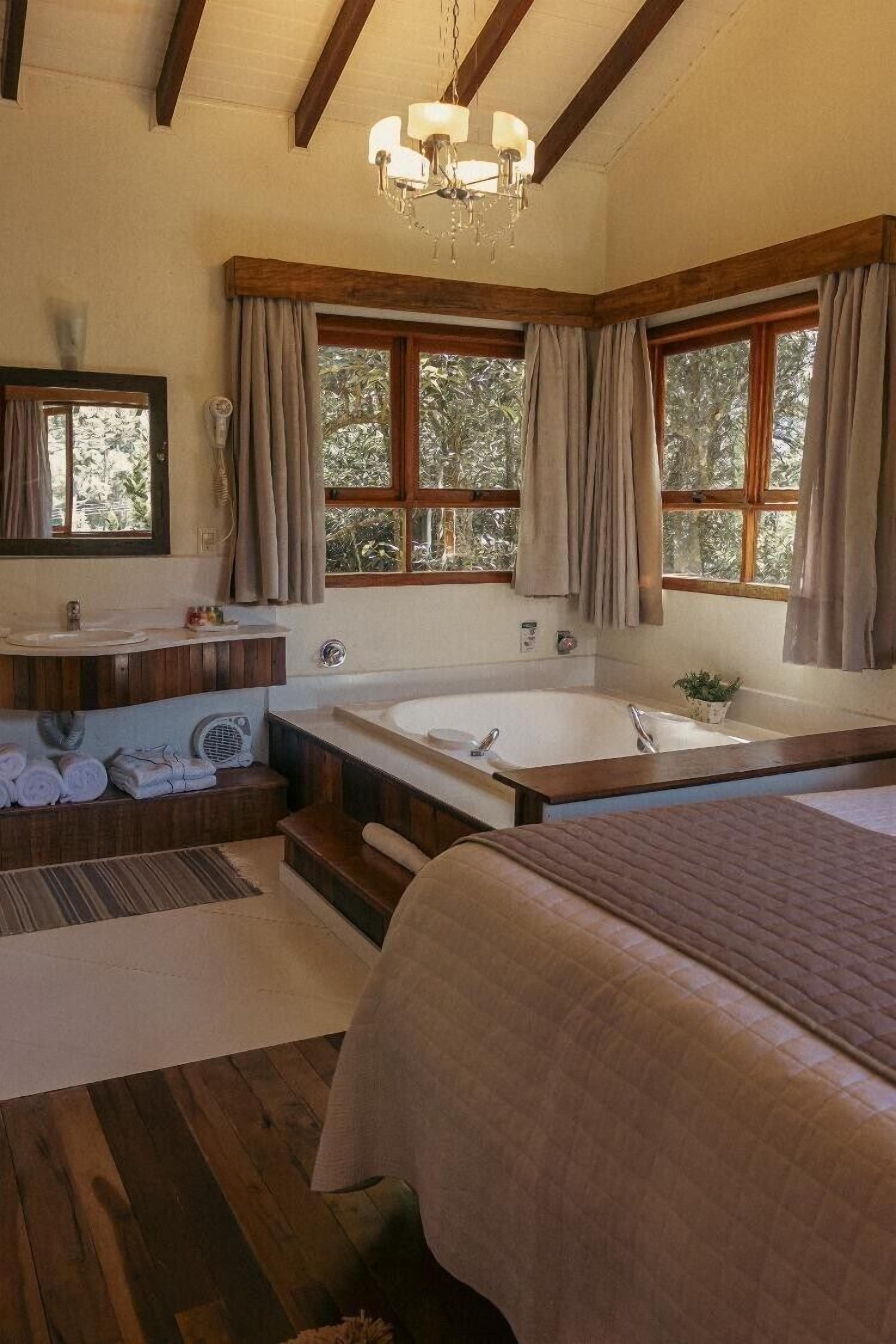 Une chambre spacieuse avec un grand lit, une salle de bain séparée avec une baignoire et une grande fenêtre avec des rideaux.
