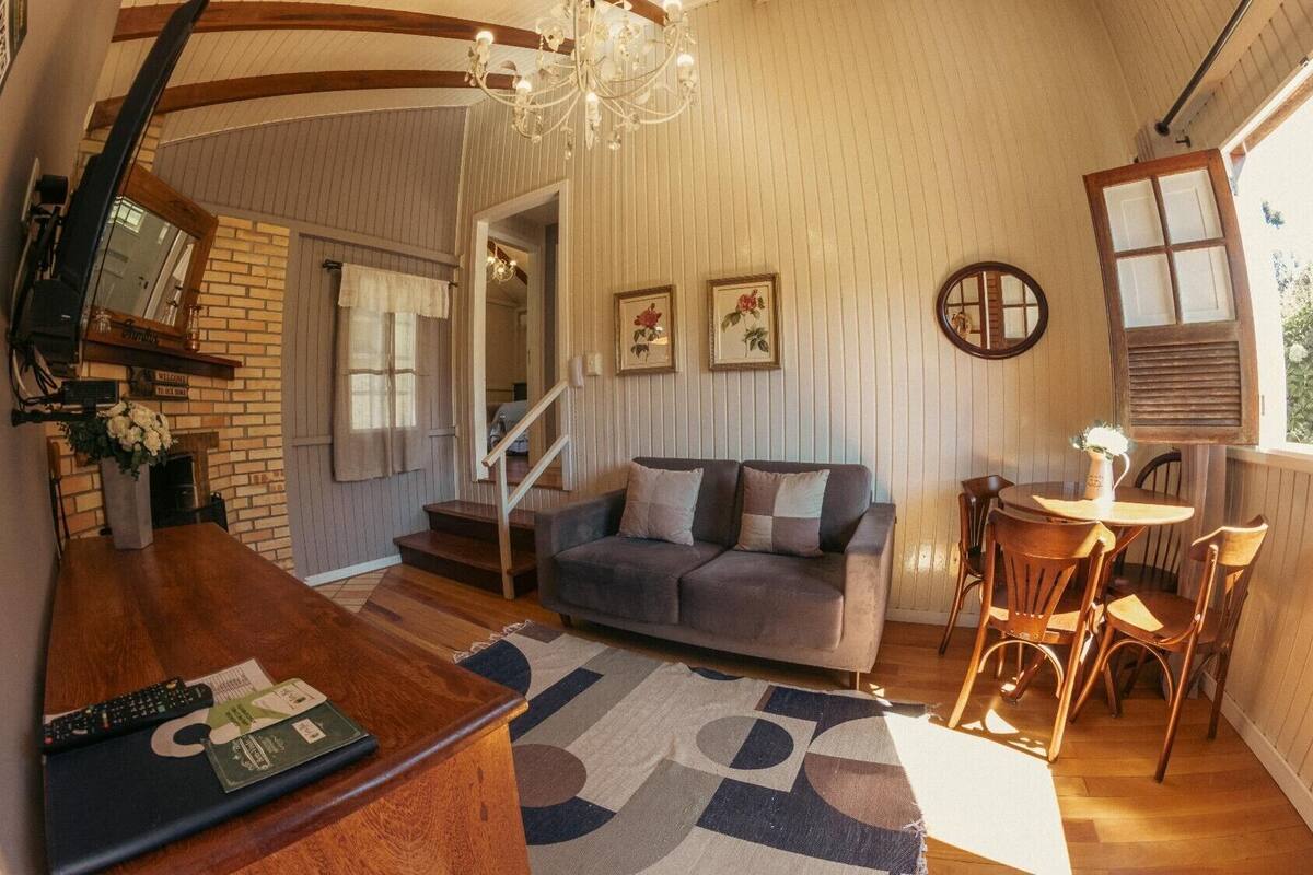 A cozy living room with a sofa, a dining table with chairs, a fireplace, and a staircase leading to another level.