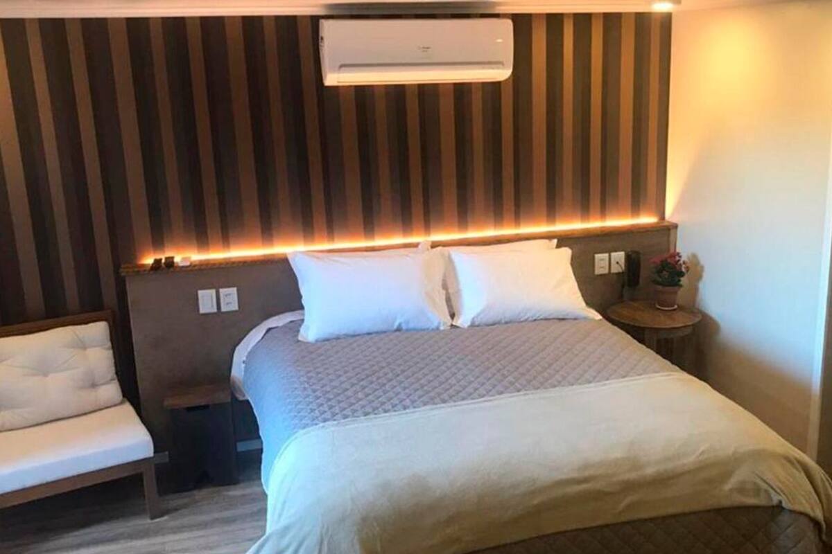 A hotel room with a bed, bedside tables, a chair, and a wall-mounted air conditioner.