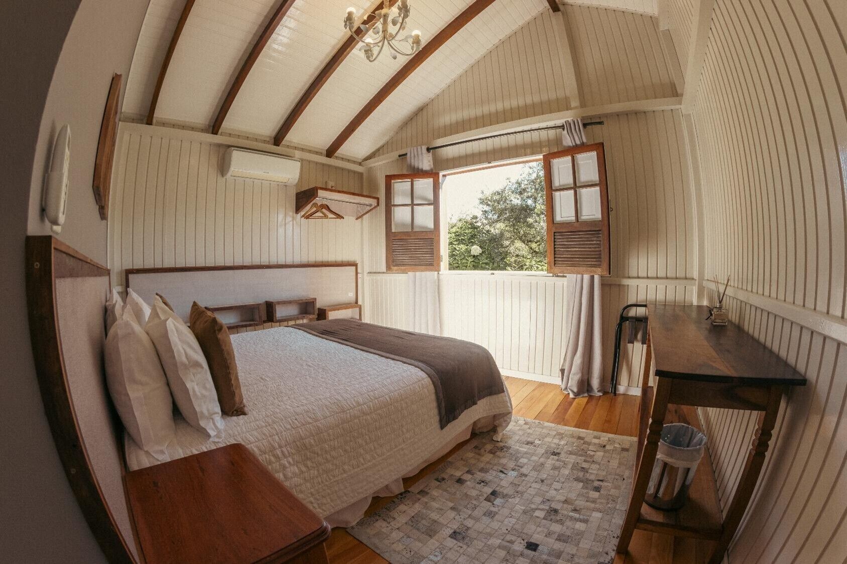 A bedroom with a wooden bed, a nightstand, a desk, and a window with shutters.