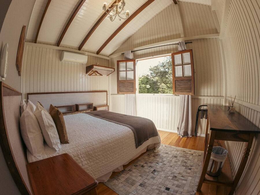 A bedroom with a wooden bed, a nightstand, a desk, and a window with shutters.