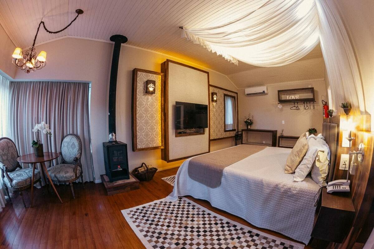 A hotel room with a bed, a television, a fireplace, a dining area, and a chandelier.