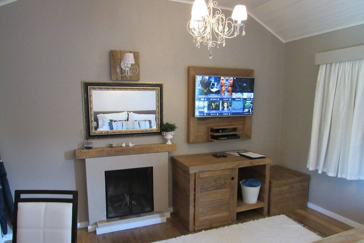 A living room with a fireplace, a mounted TV, a chandelier, and a wooden cabinet.