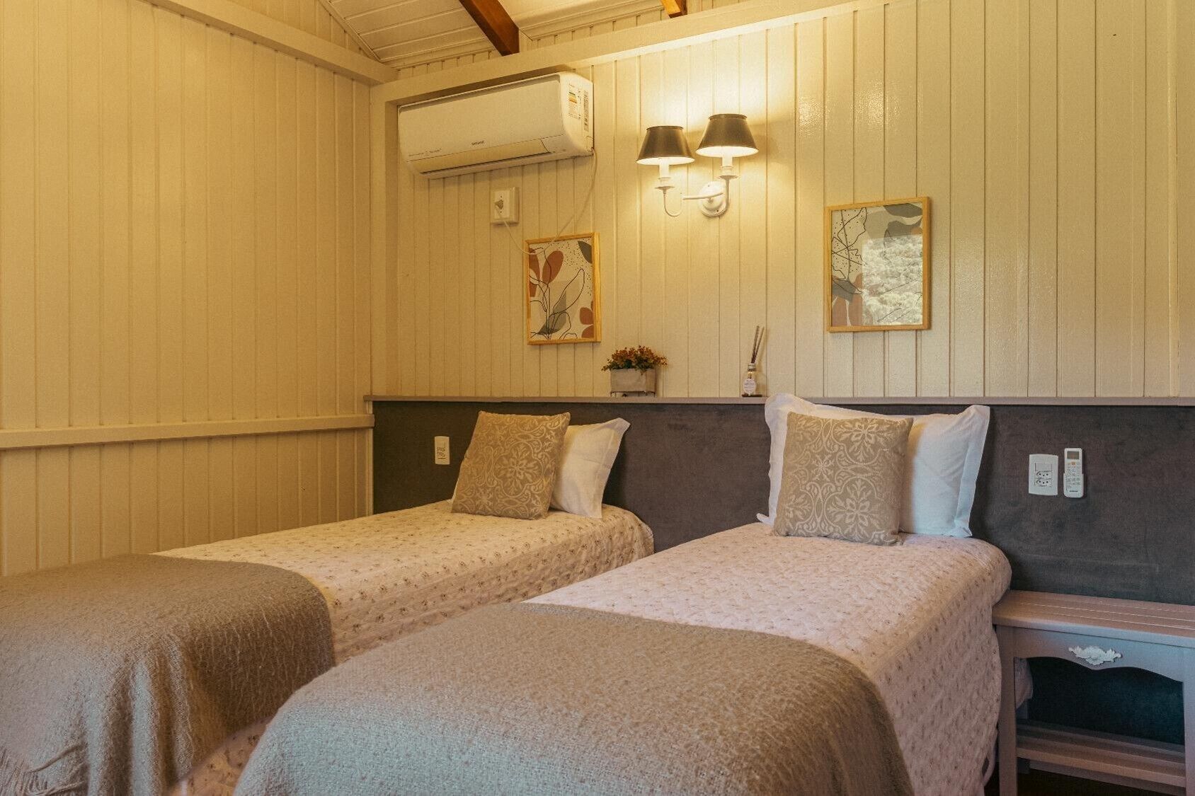 Una habitación con dos camas, aire acondicionado de pared, dos apliques y una mesita con lámpara.