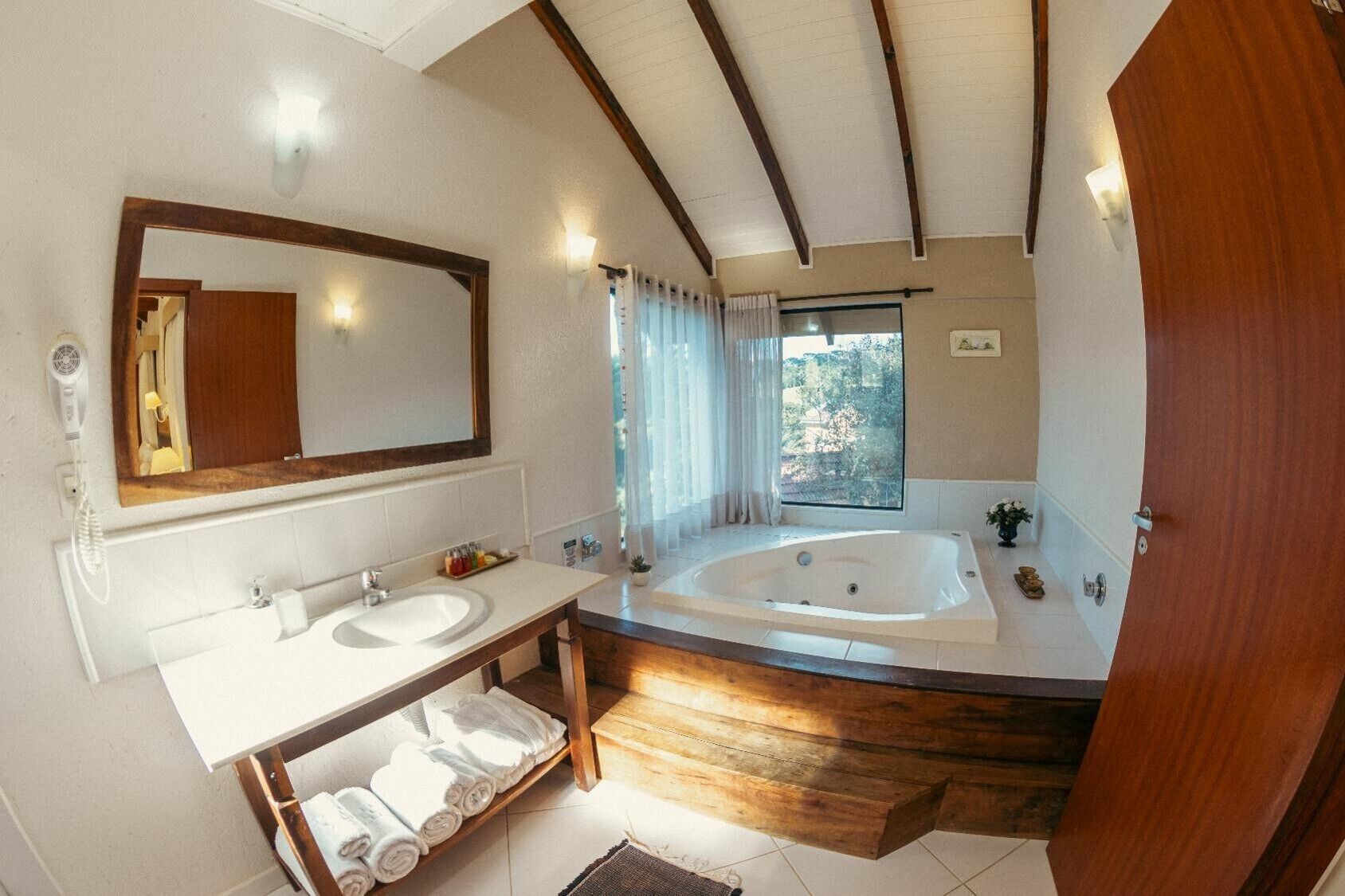 A bathroom with a large bathtub, two sinks, a mirror, and a window with curtains.