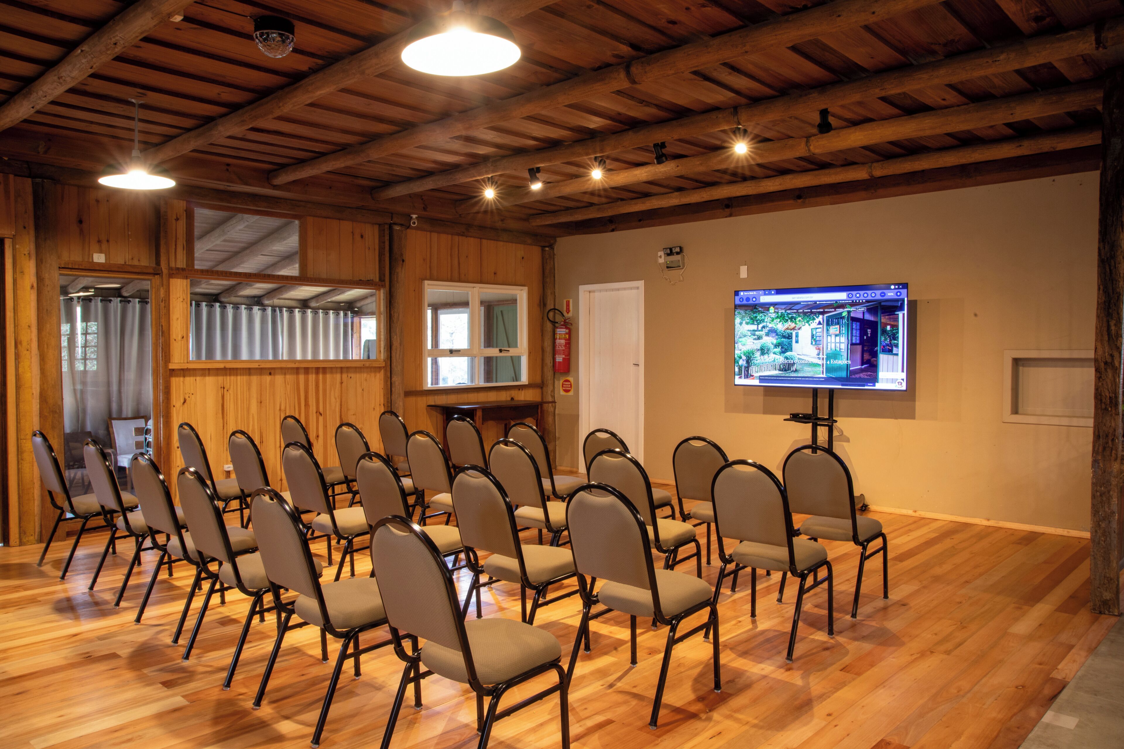Un salón de conferencias con suelos de madera, filas de sillas, una pantalla grande y vigas de madera en el techo.