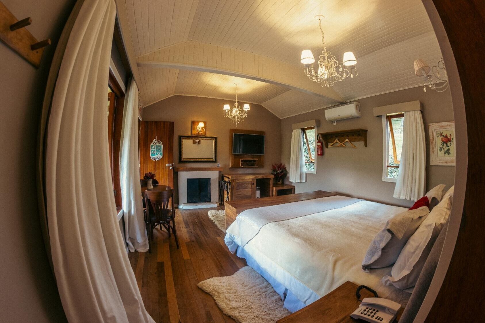 A bedroom with a large bed, a fireplace, a chandelier, and a television.