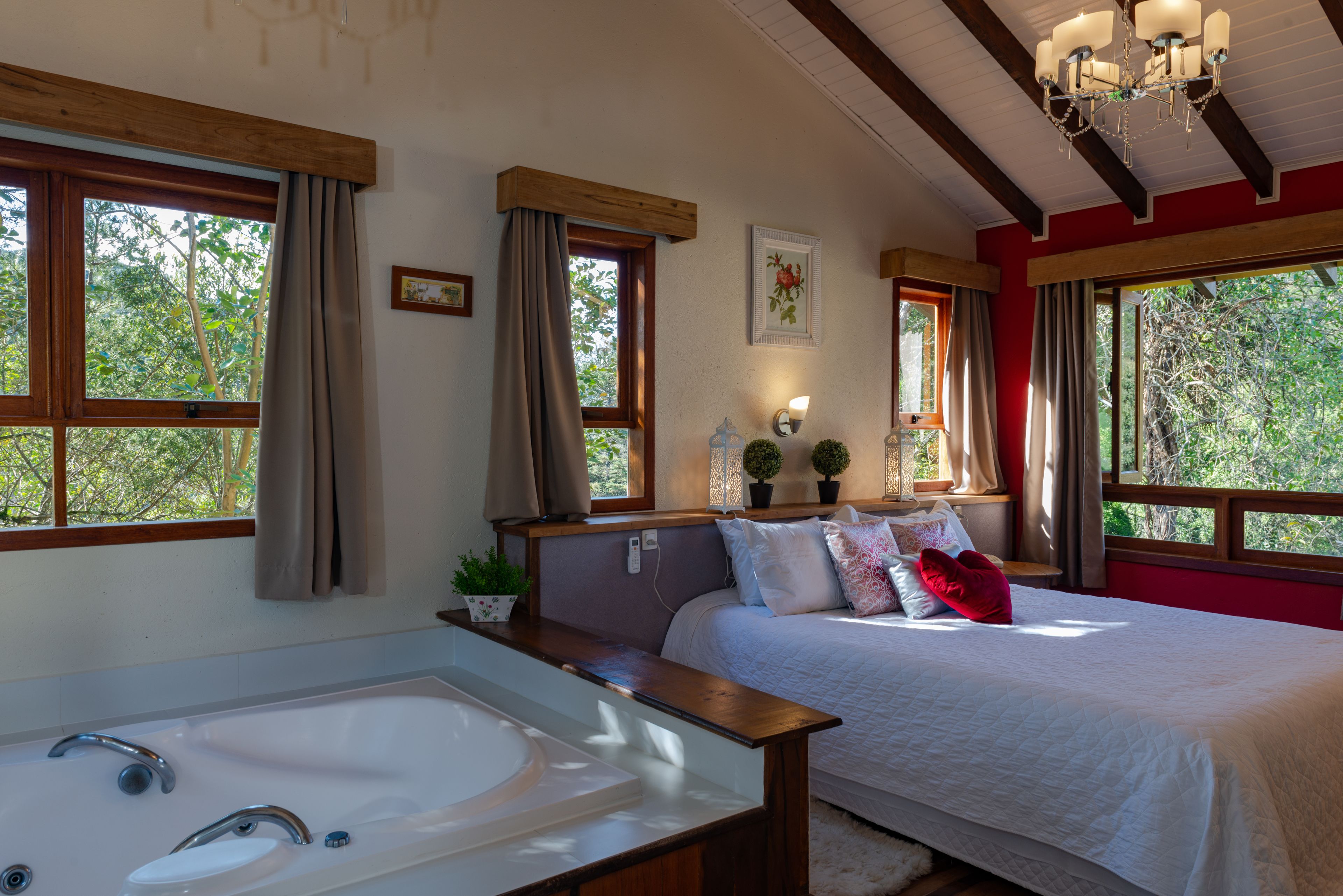 A bedroom with a large bed, a wooden headboard, a bedside table, a nightstand, a lamp, and a window with curtains.