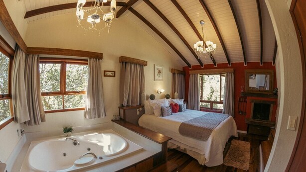 Une chambre spacieuse avec un grand lit, une salle de bain séparée avec une baignoire, un plancher en bois et une cheminée.