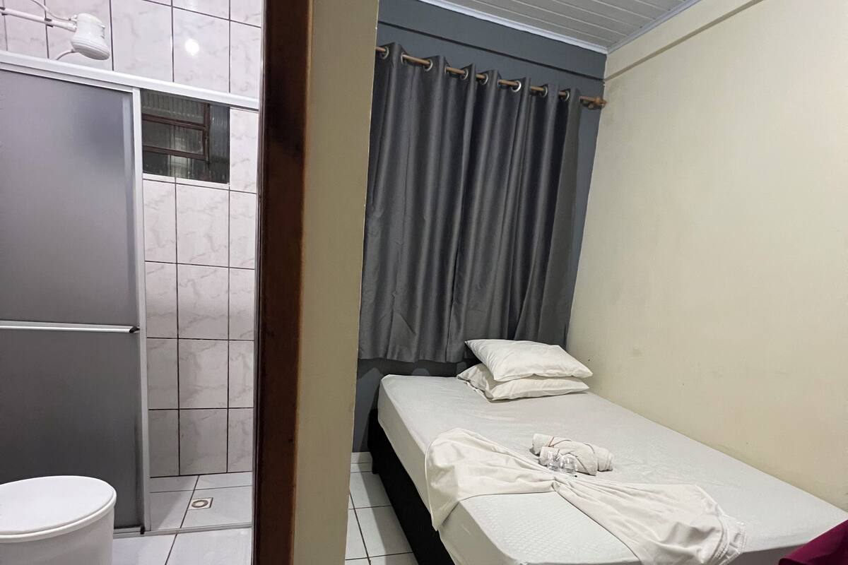 A small, clean room with a bed, a toilet, and a shower area.