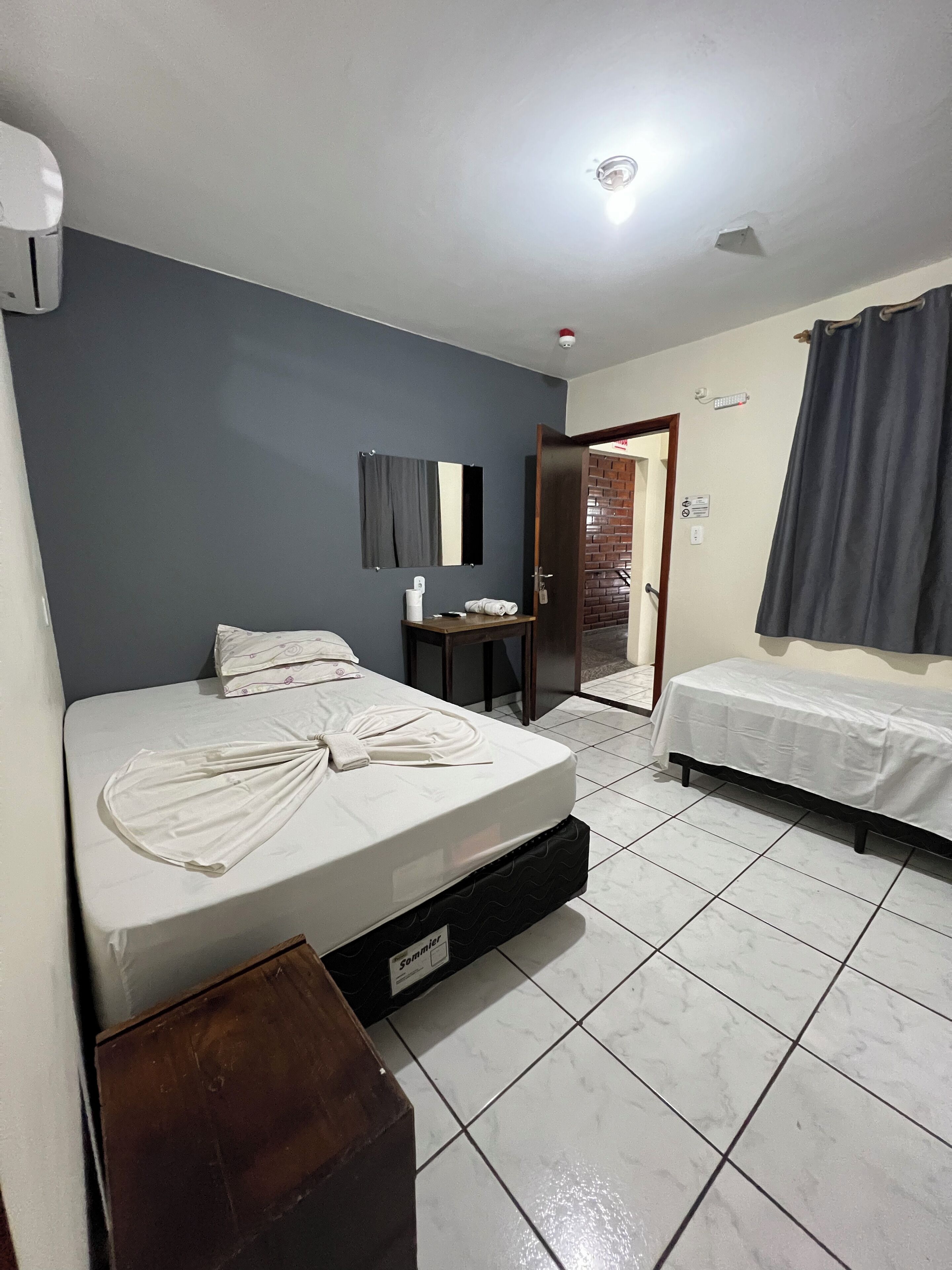 Une chambre d’hôtel avec un lit, un petit bureau, un miroir et une porte donnant sur une autre pièce.