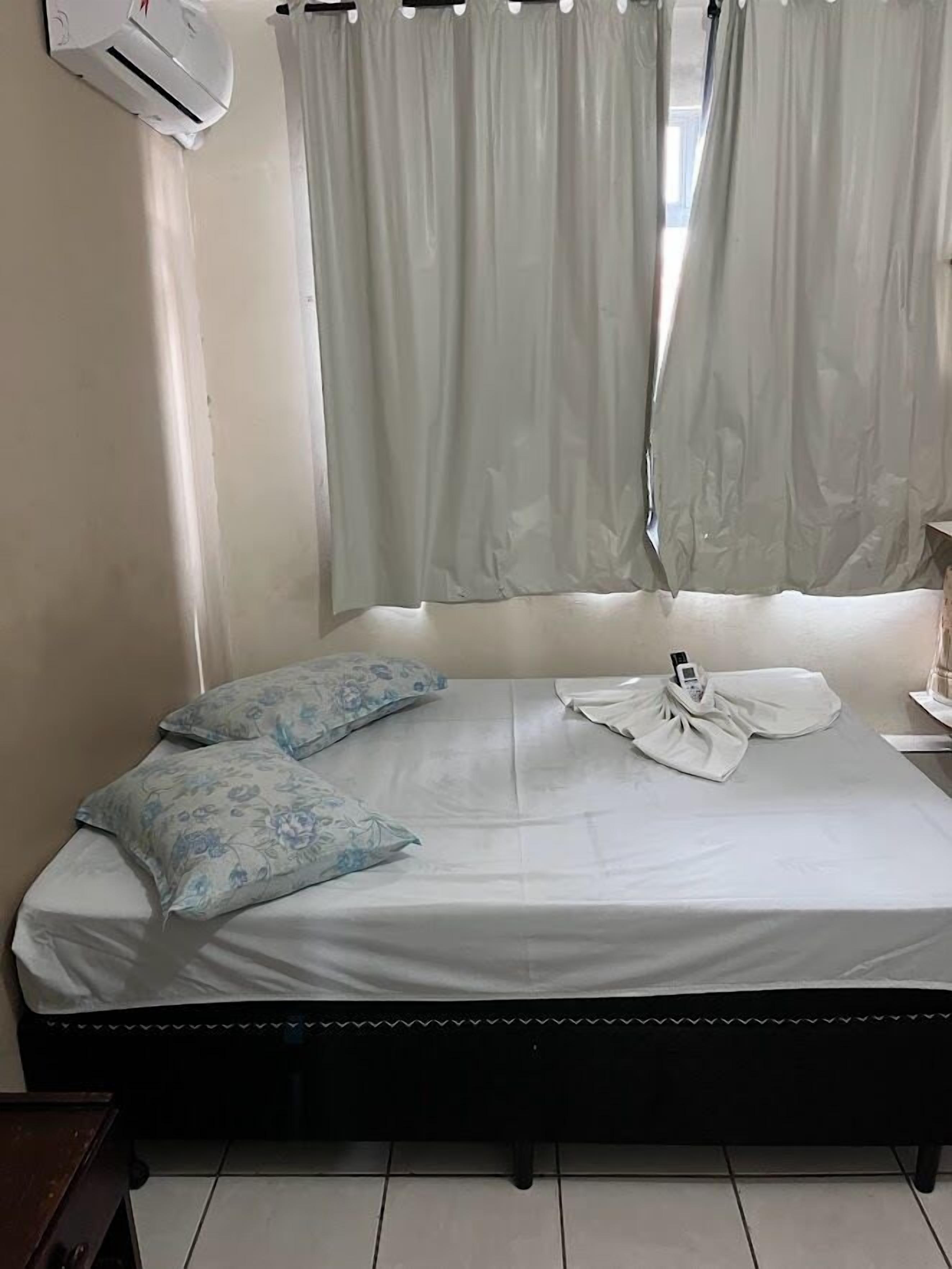 A neatly made bed with floral pillows, a white blanket, and a folded white shirt on the bed.