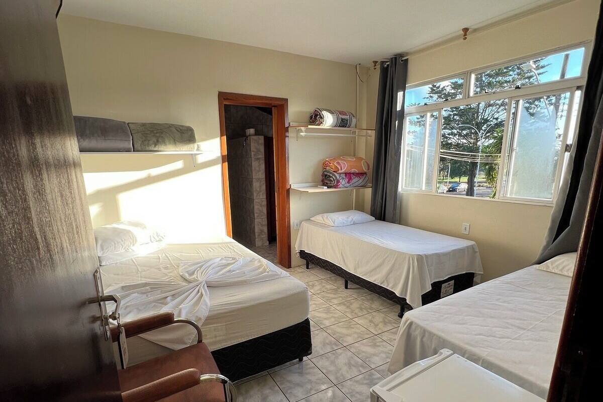 A hotel room with two beds, a shower, a small table, and a window with a view of trees.