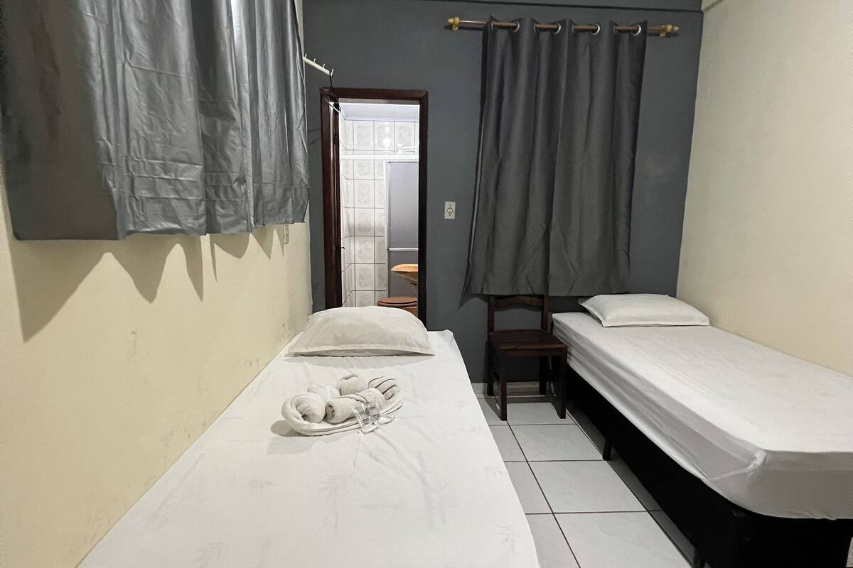 A room with two single beds, a small table with a towel and slippers, and a chair.