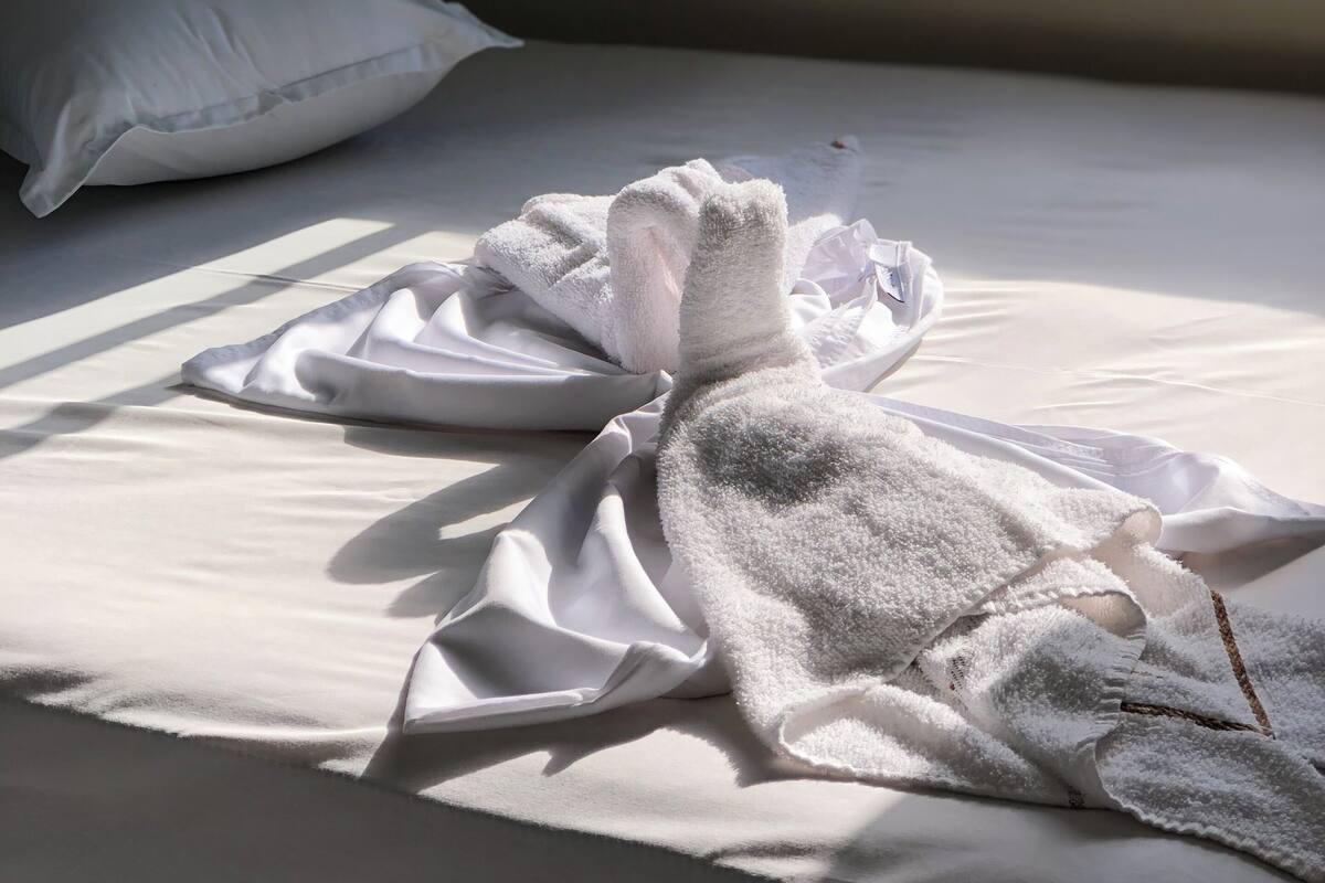 A bed with white linens and a folded towel on it.