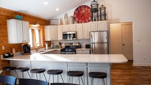 A modern kitchen with white cabinets, a large island with bar stools, stainless steel appliances, and a red clock.