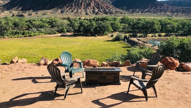 An outdoor seating area with chairs and a fire pit, overlooking a scenic landscape with mountains and a river.