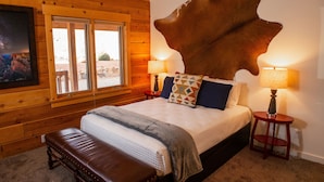 A bedroom with a large wooden headboard, a bed with multiple pillows, a bench, and two bedside lamps.
