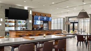 Un espace bar moderne doté d’un long comptoir, de nombreux sièges et d’un grand écran affichant le menu.