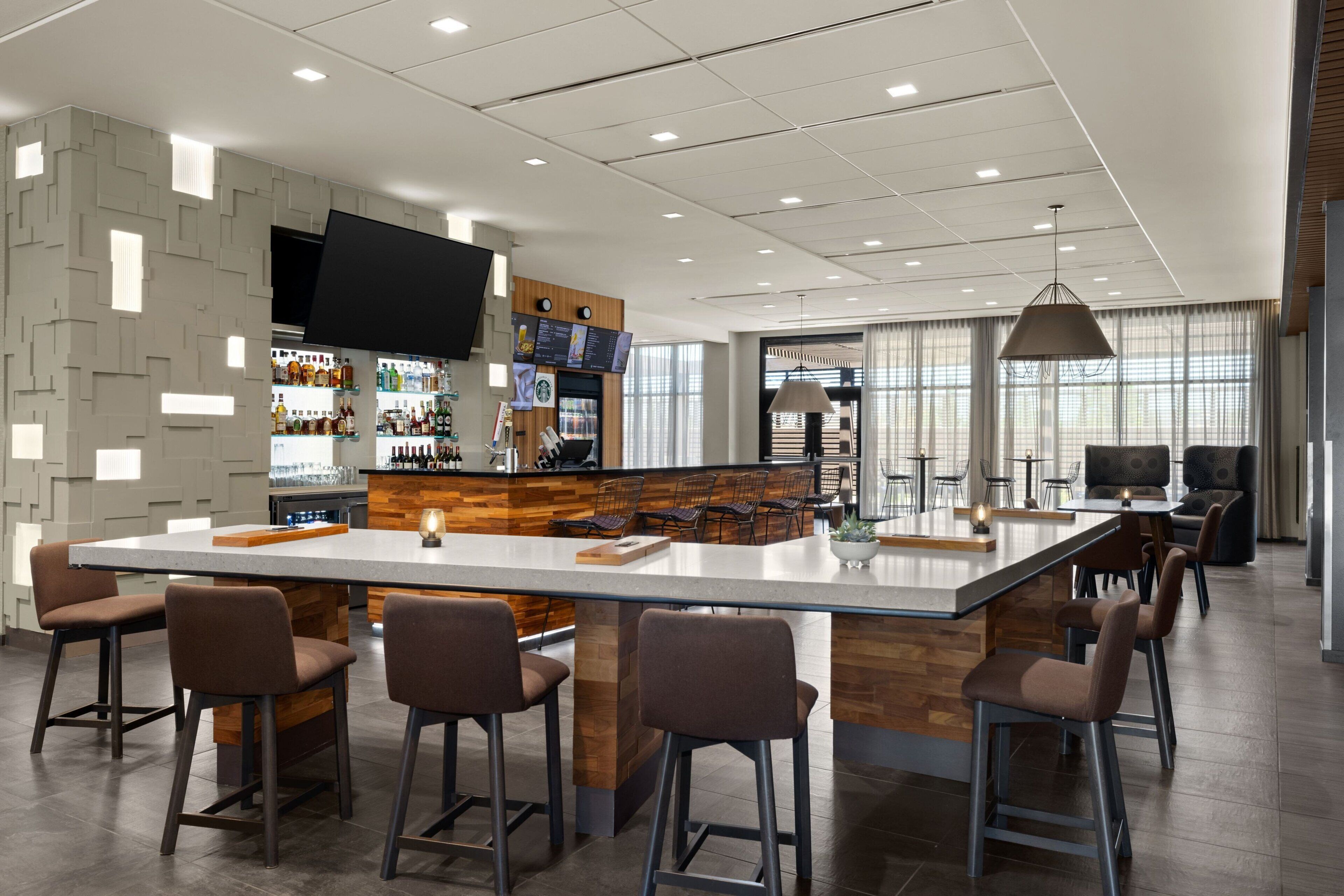 A modern bar area with a large island, bar stools, and a television screen.