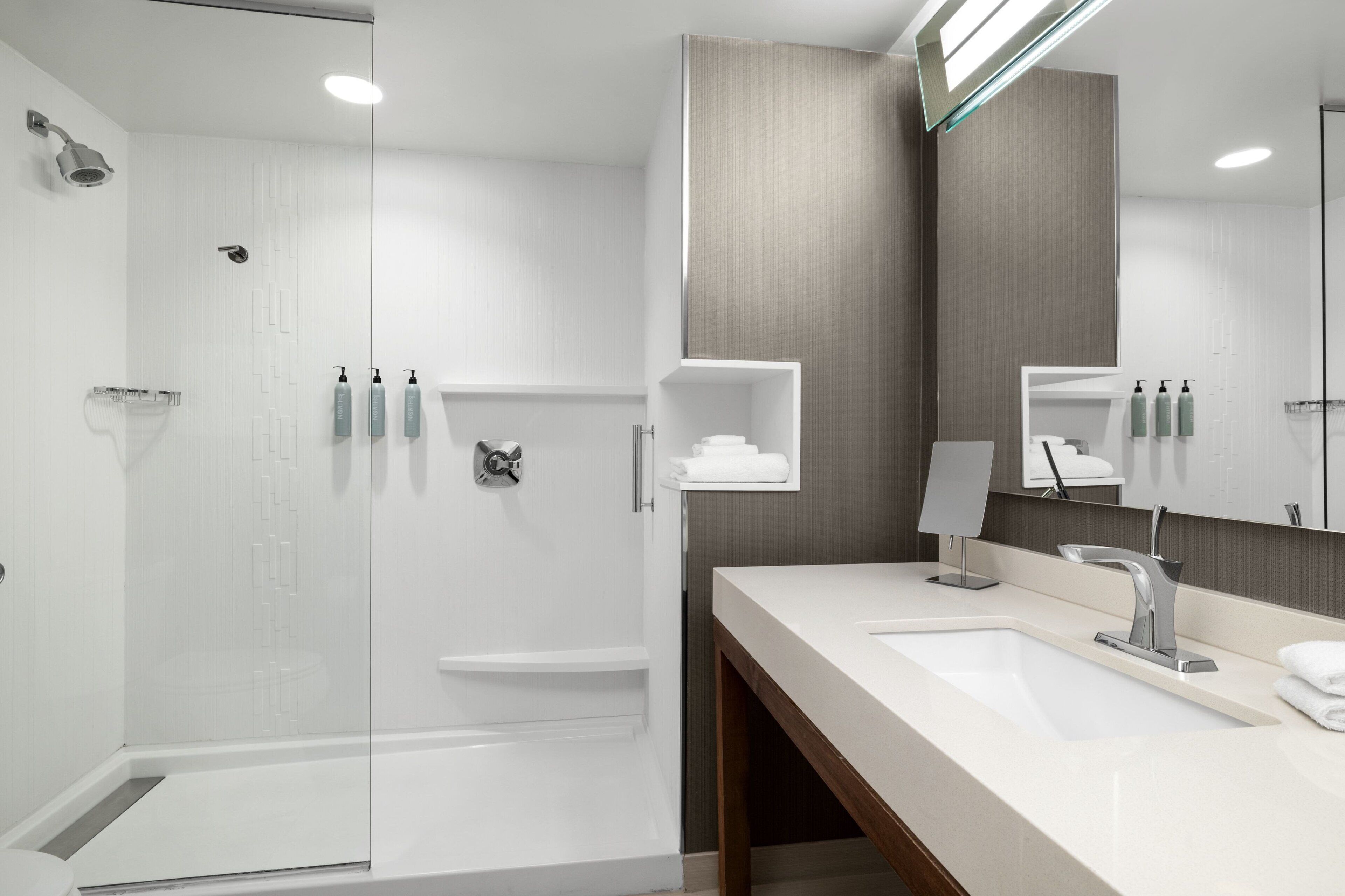 A modern bathroom with a glass-enclosed shower, a large mirror, and a vanity with a sink and towel rack.