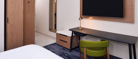 A hotel room with a bed, a desk with a chair, a TV, a wardrobe, and a mirror.