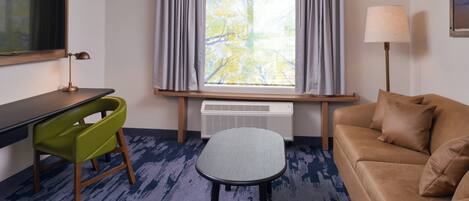 A hotel room with a desk, green chair, sofa, and a window with curtains.