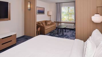 A hotel room with a bed, a sofa, a small table, a TV, a lamp, and a window with curtains.