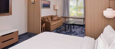 A hotel room with a bed, a sofa, a small table, a TV, a lamp, and a window with curtains.