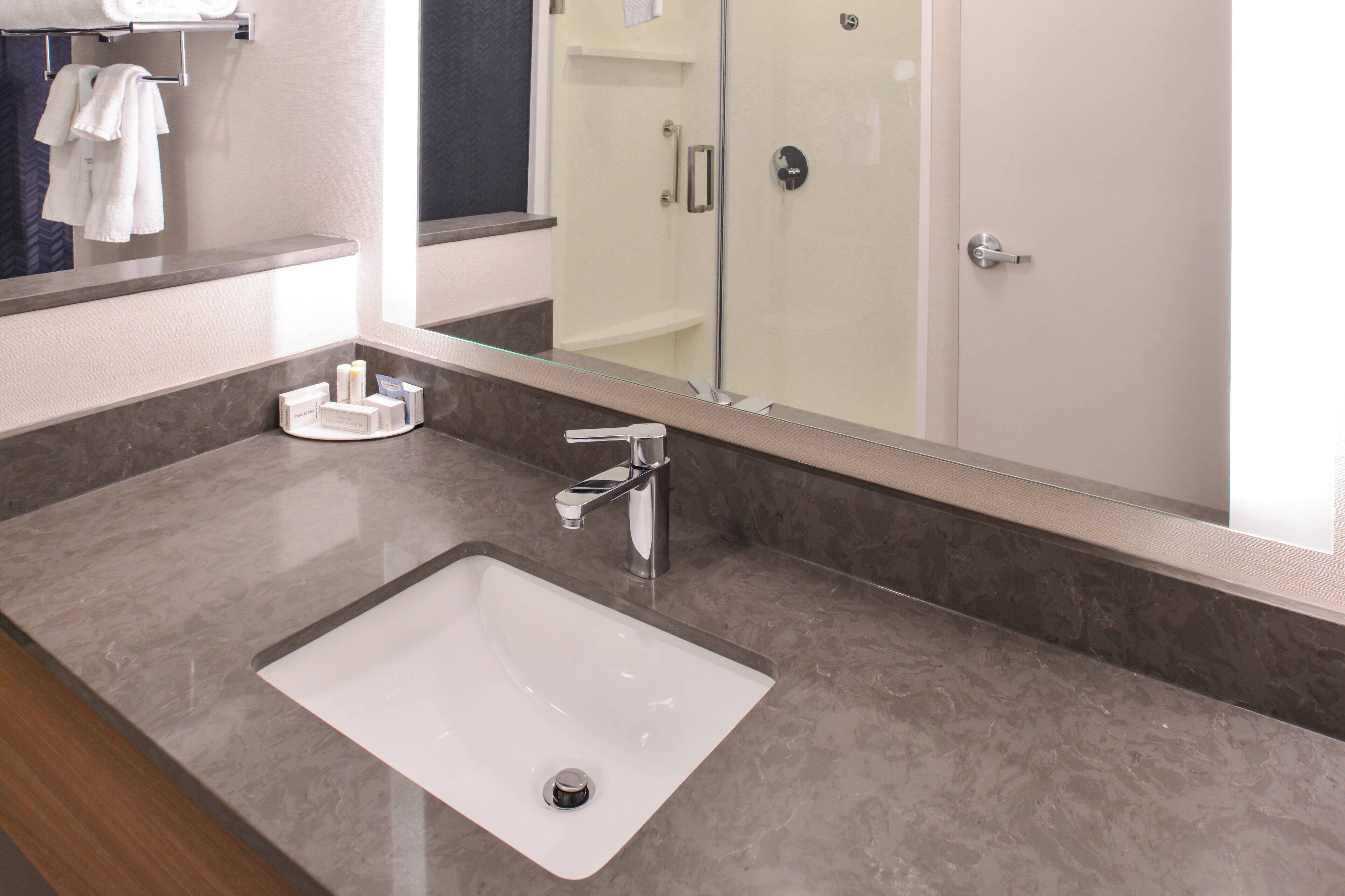 A modern bathroom with a large mirror, a white sink, and a shower area.