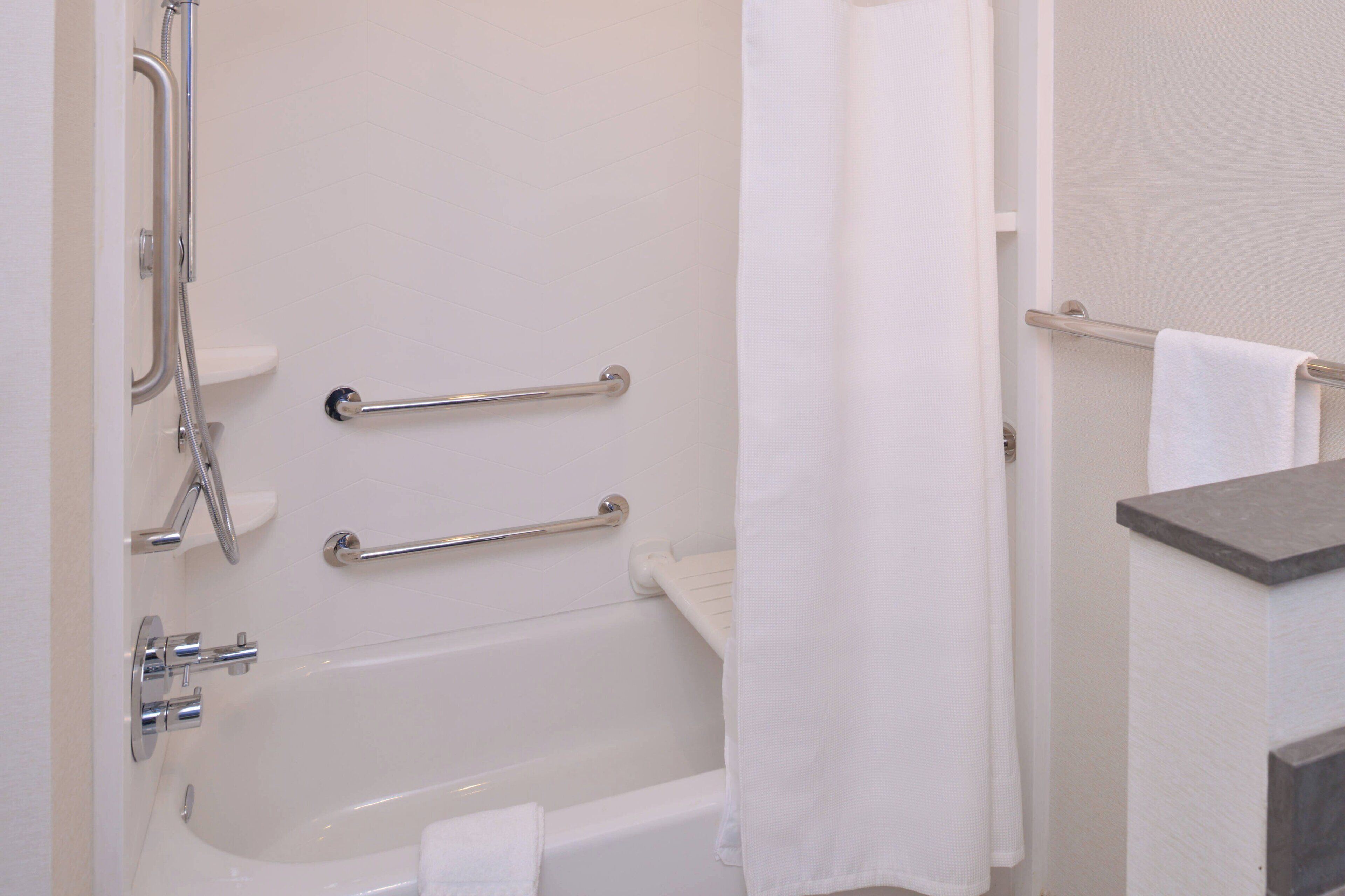 Ein Badezimmer mit Badewanne, Haltegriffen, Dusche und Handtuchhalter.