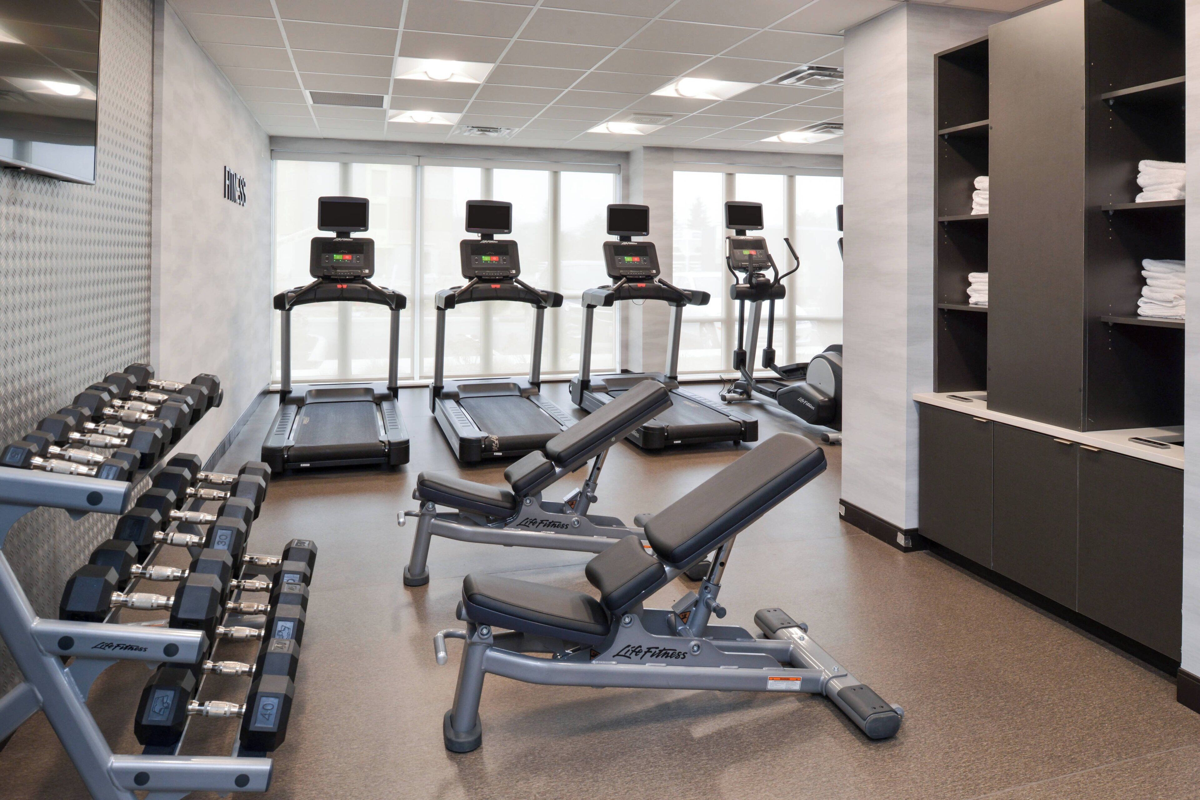 Une salle de sport équipée de tapis de course, d’haltères et de bancs de musculation.