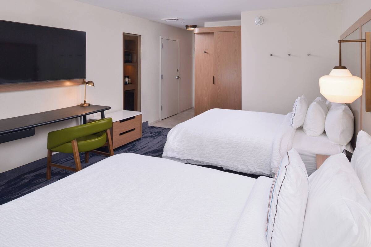 Une chambre d’hôtel avec deux lits, un bureau, une chaise, une télévision et une armoire.
