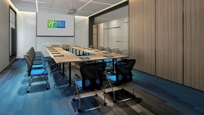 Une salle de conférence équipée d’une longue table, de chaises, d’un écran de projection et d’un mur recouvert de panneaux en bois.