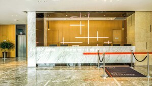 Un comptoir d’accueil avec un revêtement en marbre, un mur recouvert de panneaux en bois, une plante en pot et un espace recouvert d’une moquette rouge réservé aux membres privilégiés.