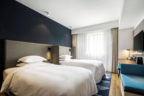Une chambre d’hôtel avec deux lits, un bureau avec une chaise, un téléviseur à écran plat et une fenêtre avec des rideaux.