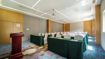 A conference room with a podium, rows of tables with green tablecloths, white chairs, and a patterned carpet.