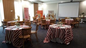A conference room with round tables covered in red and white striped tablecloths, wooden chairs, and floral centerpieces.