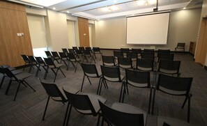 A conference room with rows of chairs and a large projection screen.