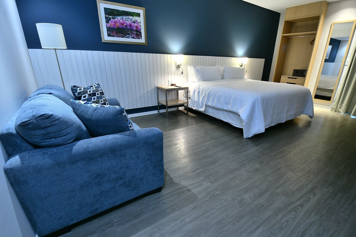 A hotel room with a bed, a sofa, a bedside table, a lamp, and a wardrobe.