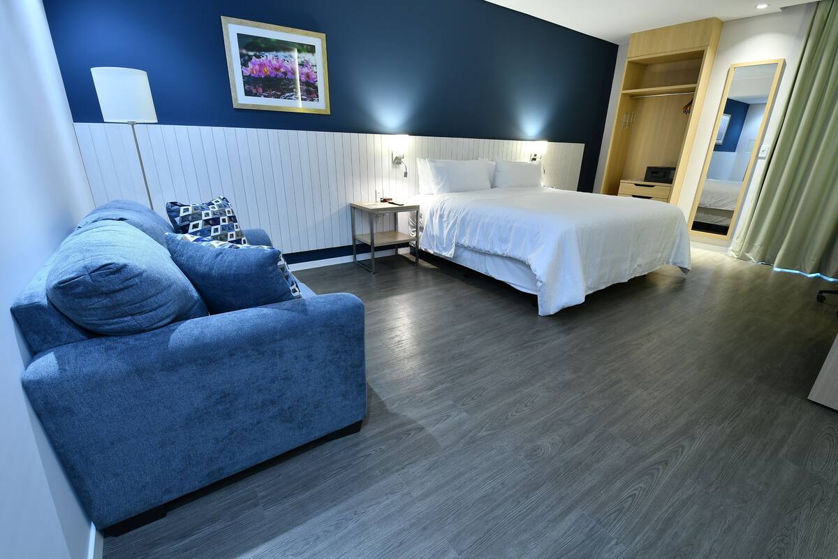 A modern hotel room with a blue sofa, a bed, a bedside table, and a wardrobe.