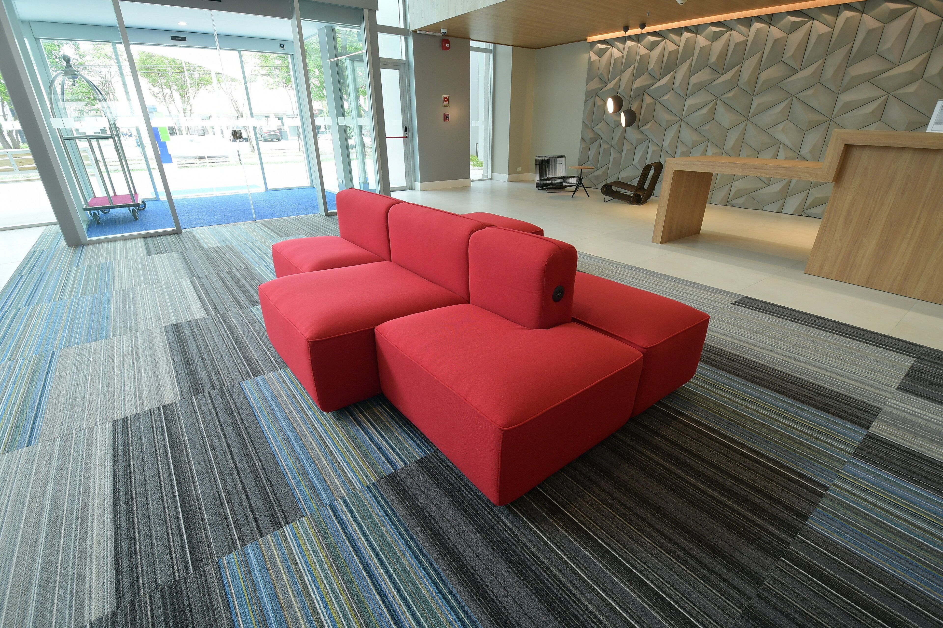 A modern lobby with a red sectional sofa, a reception desk, and a patterned wall.