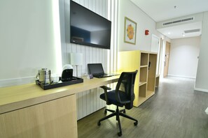 A modern office space with a wooden desk, a black office chair, a flat-screen TV, a coffee machine, and a laptop.