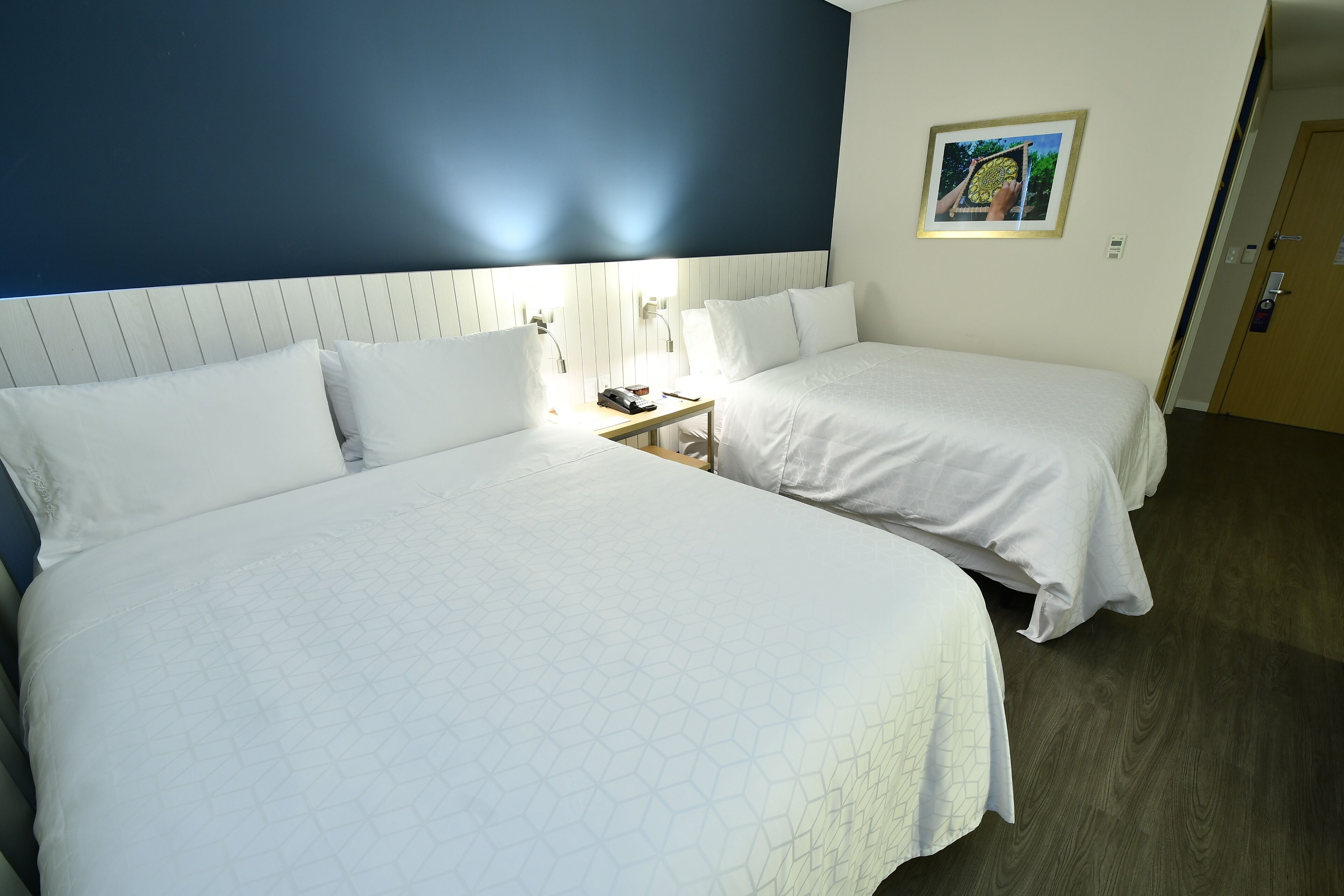 A hotel room with two beds, a nightstand, and a framed picture on the wall.