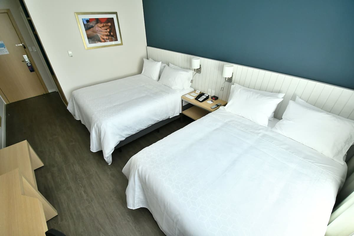 A hotel room with two beds, a nightstand with a phone and lamp, and a picture on the wall.