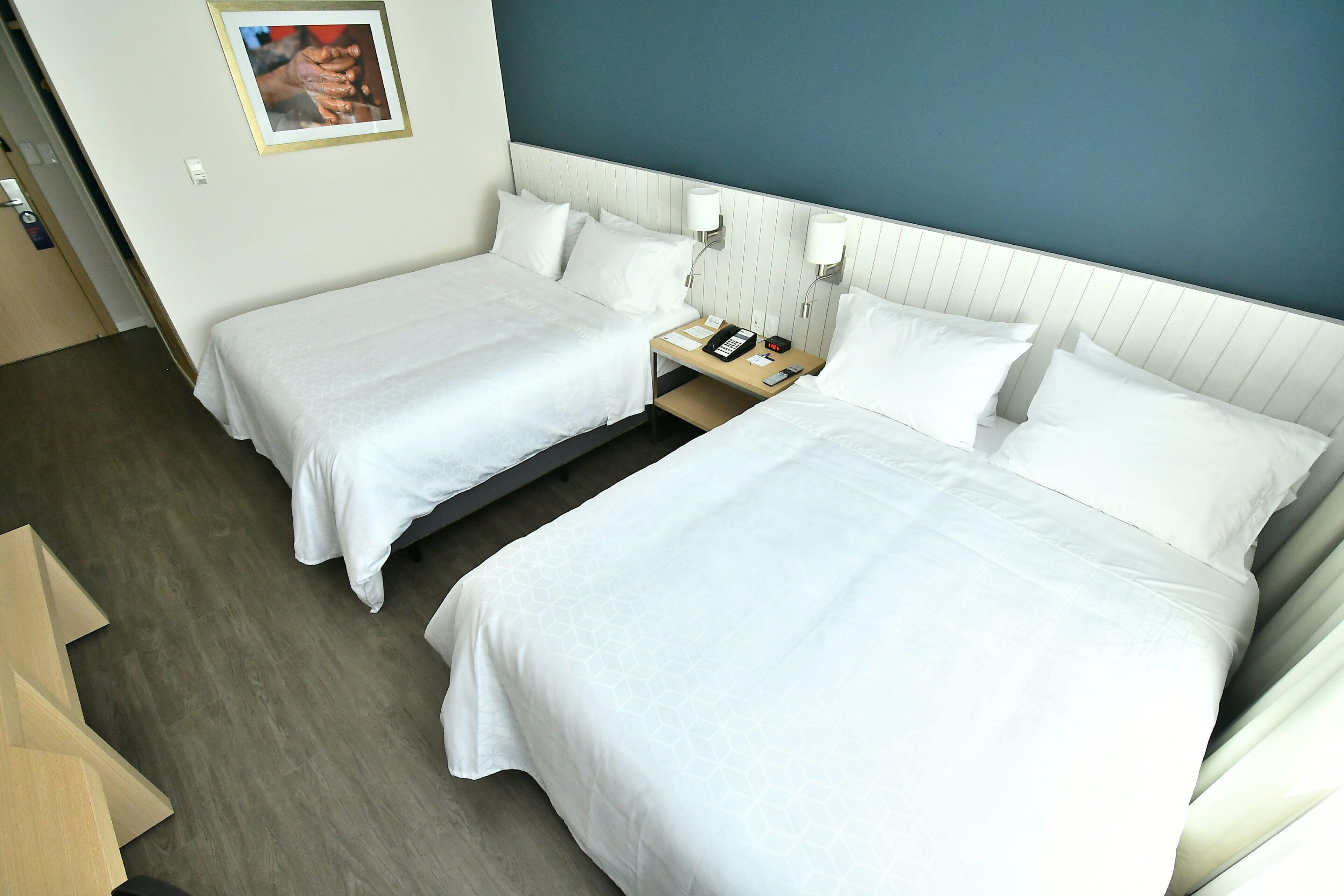 A hotel room with two single beds, a bedside table with a phone and a lamp, and a picture on the wall.